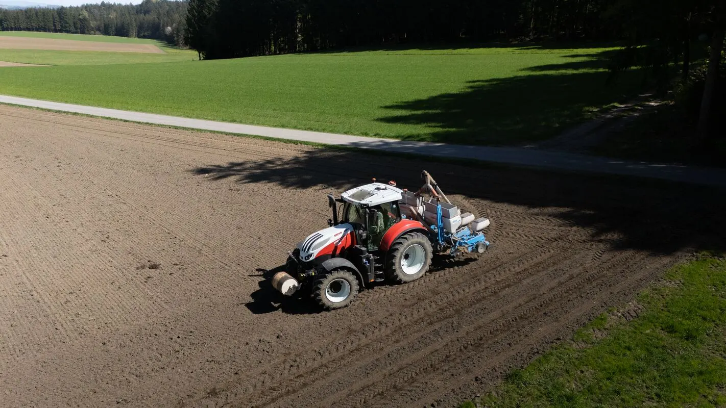 Traktor mit Sämaschine am Waldrand, Luftaufnahme